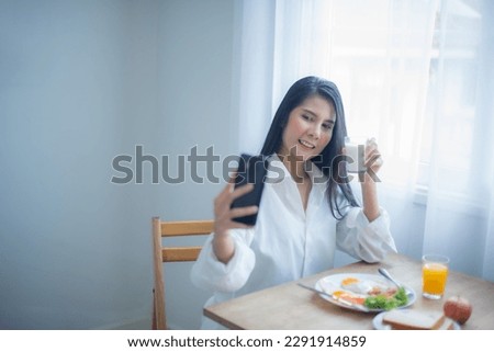 Beautiful young asian woman holding a cell phone taking a selfie of herself with breakfast while holding a glass of milk.