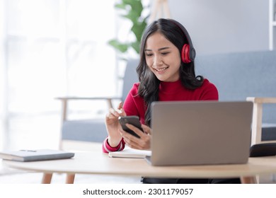 Beautiful Young asian woman at home sitting on the sofa while using laptop phone and headphone listening to music at home