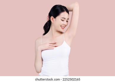 Beautiful young Asian woman lifting hand up to shows off clean and clear armpit or underarms isolated on pink background, Smooth and freshness armpit concept.