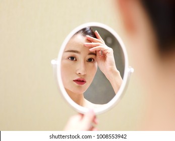 Beautiful Young Asian Woman Looking At Self In Mirror, Hand On Forehead.