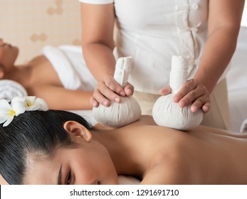 Beautiful young asian woman lying on the bed having a massage with herbal compresses in a spa. Thai massage for health. Select focus hand of masseuse
