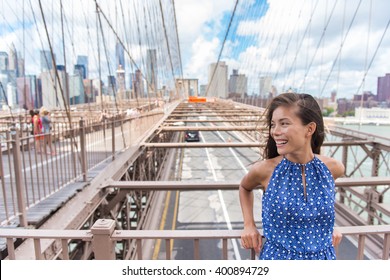 Beautiful Young Asian Woman Portrait On Brooklyn Bridge, New York City NYC, Manhattan, USA. Smiling Tourist In Blue Dress Doing Summer Travel In Urban Landmark.