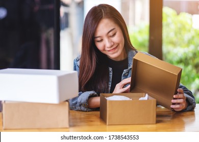 A beautiful young asian woman receiving and opening a postal parcel box at home for delivery and online shopping concept - Powered by Shutterstock