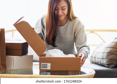 A beautiful young asian woman receiving and opening a postal parcel box at home for delivery and online shopping concept