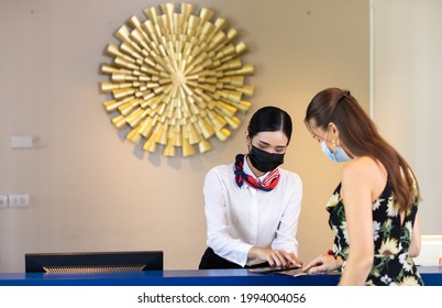 beautiful young asian woman receptionists working at a reception desk and holding key card or passport to customer. People wearing protective face mask prevent covid-19 virus  - Powered by Shutterstock