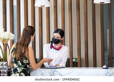 beautiful young asian woman receptionists working at a reception desk and holding key card or passport to customer. People wearing protective face mask prevent covid-19 virus  - Powered by Shutterstock