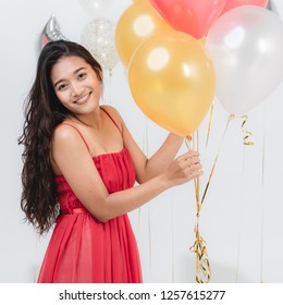 Beautiful Young Asian Woman In Red Dress, Happy Smiling At Fun Party While Holding Colorful  Balloons. Studio Portrait Shot On White Background.