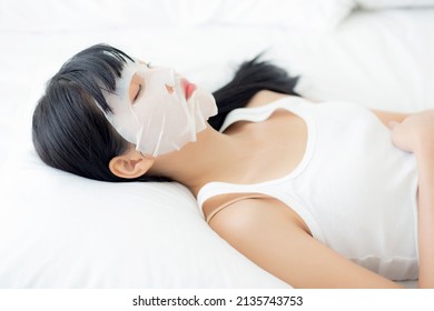 Beautiful Young Asian Woman With Sheet Facial Mask And Sleep On Bed At Bedroom, Beauty Girl Applying Cosmetic And Makeup With Skin Care Face For Wrinkle, Skincare Treatment, Health And Wellness.