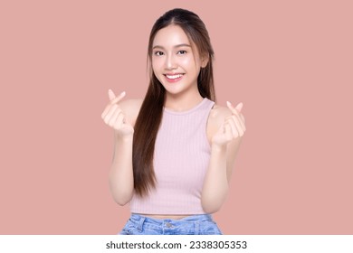 Beautiful young Asian woman shows mini heart fingers on isolated pink background. Facial and skin care concept for commercial advertising.