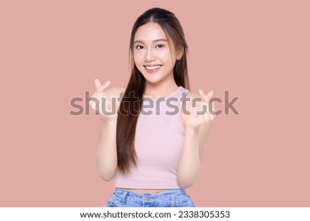 Beautiful young Asian woman shows mini heart fingers on isolated pink background. Facial and skin care concept for commercial advertising.