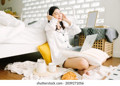 Beautiful Young Asian Woman Sitting Next To Her Bed Using Her Laptop And Enjoy Breakfast In The Morning At Home. Small Business Owners Are Checking Orders Online. Concept For Freelancer Lifestyle.