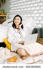 Beautiful Young Asian Woman Sitting Next To Her Bed Using Her Laptop And Enjoy Breakfast In The Morning At Home. Small Business Owners Are Checking Orders Online. Concept For Freelancer Lifestyle.