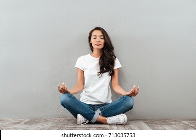 Beautiful young asian woman sitting in yoga position and meditating isolated over gray background - Shutterstock ID 713035753