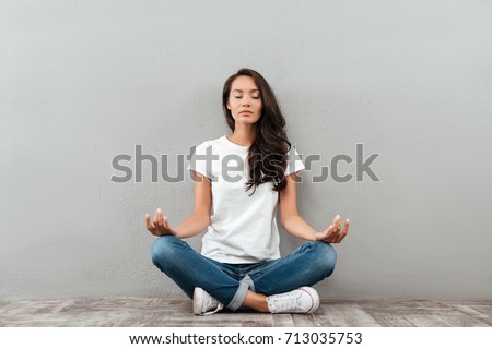 Beautiful young asian woman sitting in yoga position and meditating isolated over gray background