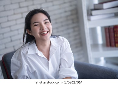 beautiful young asian woman smiling while sitting on the chair against white brick wall - Shutterstock ID 1752627014