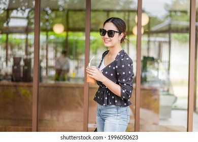 Beautiful young Asian woman smiling face hand holding takeaway ice coffee cup in front of cafe or restaurant, Portrait of happy attraction traveler girl in sunglasses on street, Lifestyle Asia people 