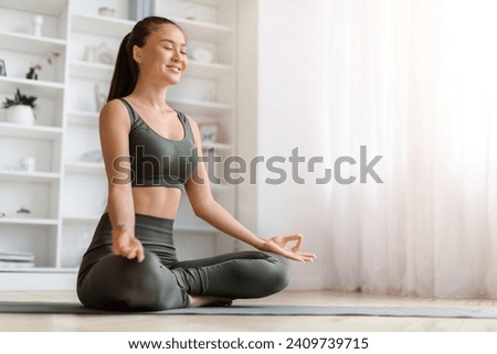 Beautiful young asian woman smiling gently while practicing yoga at home, calm korean female meditating on mat in living room, performing mudra, embodying relaxation and joy, copy space