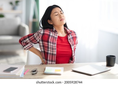 Beautiful Young Asian Woman Suffering From Backache While Sitting At Desk In Home Office, Tired Korean Freelancer Lady Having Acute Lower Back Pain After Long Time Working With Laptop Computer