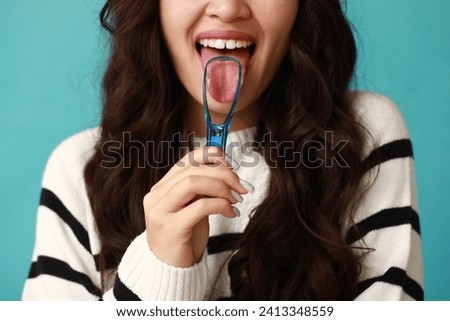 Beautiful young Asian woman with tongue scraper on blue background