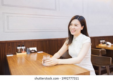 Beautiful young asian woman in traditional white dress named cheongsam sitting in Japanese restaurant or cafeteria and waiting ordered food. Happy person celebrating Chinese New Year