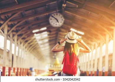 Beautiful young asian woman traveler looking clock over head with red bag ,Waiting for train at train station, Travel and vacation concept.