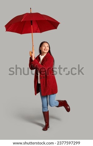 Beautiful young Asian woman with umbrella on grey background