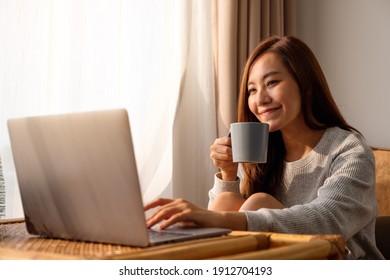 A Beautiful Young Asian Woman Using And Working On Laptop Computer While Drinking Coffee At Home