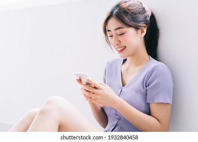 Beautiful young Asian woman using smartphone at home