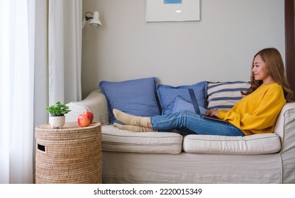 A beautiful young asian woman using and working on laptop computer while laying down on a sofa at home