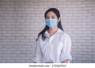 beautiful young asian woman wearing face mask to protect covid19 virus against white brick wall