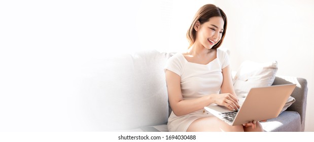 Beautiful Young Asian Woman In White T-shirt Working From Home With Laptop  In Sunshine Background By Video Call Meeting Online App. Remote Communication, Self Quarantine Prevent Coronavirus Concept.
