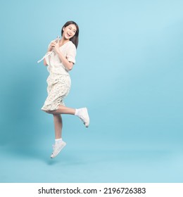 Beautiful young asian woman in white dress with flower pattern using smartphone and jump  isolated on blue background - Powered by Shutterstock