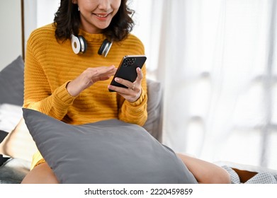 Beautiful Young Asian Woman Win Comfy Sweater Using Her Smartphone While Relaxes Sitting On Her Comfy Couch In The Living Room. Cropped Image