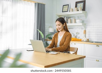 Beautiful young Asian woman working with laptop computer in home kitchen. Work at home. Remote studying, Virtual training, E-learning, Watching online education, Webinar at house - Powered by Shutterstock