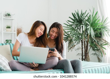 Beautiful young asian women LGBT lesbian happy couple sitting on sofa buying online using laptop a computer and phone in living room at home. LGBT lesbian couple together indoors concept. - Powered by Shutterstock