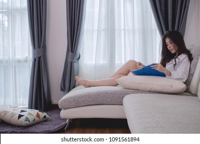 Beautiful young asian women in white shirt  reading book on modern sofa in living room. concept of young asian woman lifestyle.