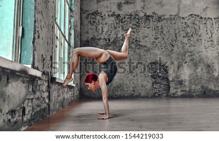 Beautiful young athletic  girl in a gray swimsuit doing a handstand near the window. Yoga concept. Gymnast doing exercises.