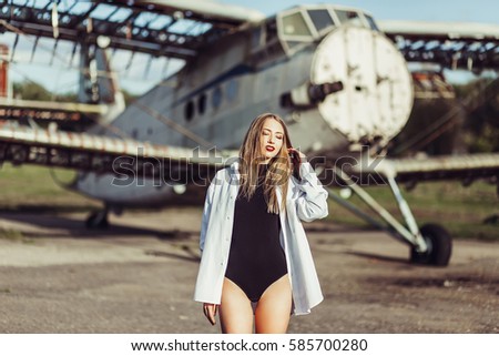 Beautiful young attractive young girl in a beautiful black body near an old airplane pleasant warm summer day in the sun