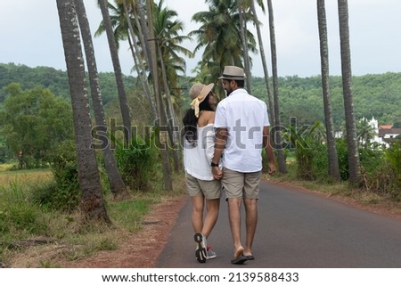 Beautiful young attractive tourist couple looking each other embracing, loving smiling cuddling walking on Parra Coconut road in Goa with palm trees fields. Love you Dear Zindagi road, valentine's day