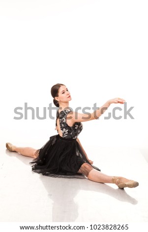 Beautiful young ballerina, isolated photo on white background. In pointes and black ballet tutu. Sits on a twine, shows different poses. Elegant brunette with long hair