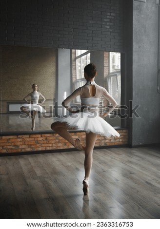Beautiful young ballerina training classic ballet in studio with huge mirror