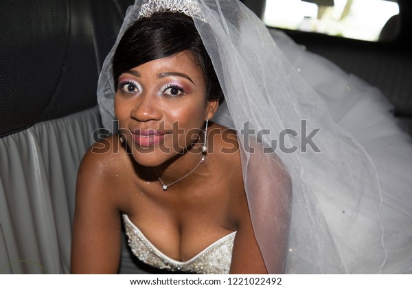 Beautiful young black bride looks at the camera and\
smiles in wedding car