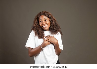 Beautiful Young Black Girl Placing Two Hands On Her Chest With An Emotional Smile While Looking Away