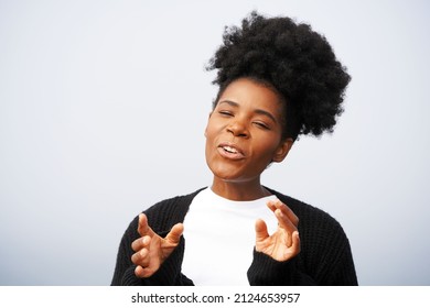 Beautiful young black woman with afro high puff ponytail hairstyle and a white shirt with black sweater talks and motions with her hands against a blue sky                              