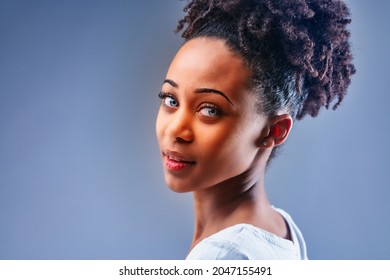 Beautiful Young Black Woman With Blue Eyes And Curly Hair Piled High On Her Head Turning To Glance Back At The Camera Over Her Shoulder In A Cropped Close Up Portrait