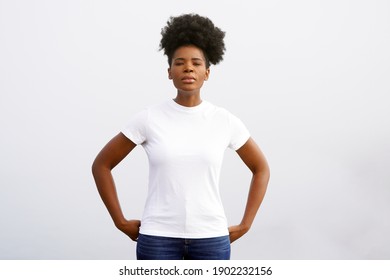 Beautiful young black woman from Cameroon wears a white shirt and stands against the sky in a striking portrait pose with an updo pony tail afro                               