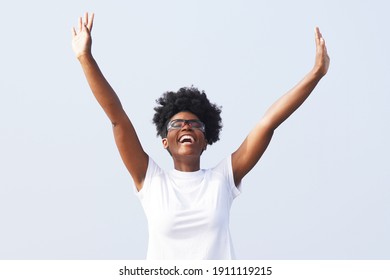 Beautiful Young Black Woman Celebrates Outdoors With Her Hands In The Air And Wearing Sporty Glasses Against A Background Of Blue Sky                              