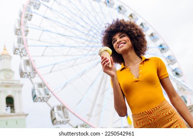 Beautiful young black woman eating ice cream at amusement park - Cheerful african-american female portrait during summertime vacation- Leisure, people and lifestyle concepts - Powered by Shutterstock