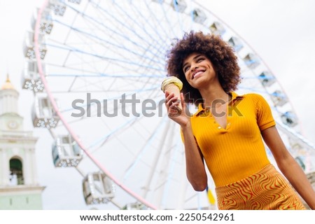 Beautiful young black woman eating ice cream at amusement park - Cheerful african-american female portrait during summertime vacation- Leisure, people and lifestyle concepts