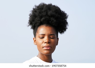 Beautiful young black woman with gorgeous skin and an updo afro pony tail stands against the blue sky outside for a closeup portrait                                - Shutterstock ID 1907358754